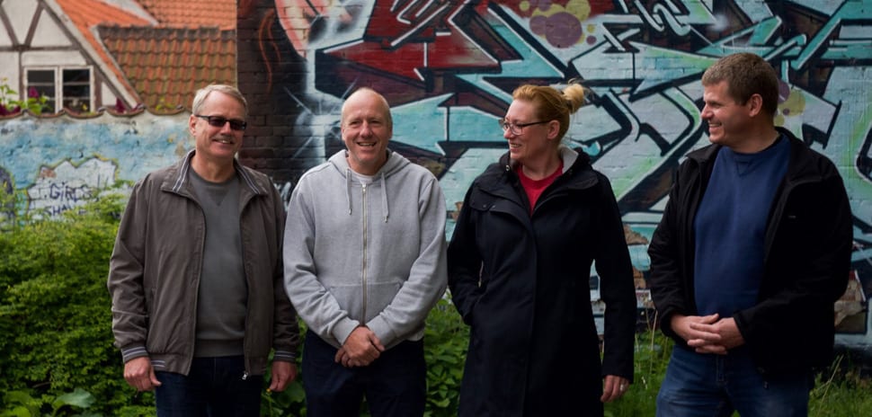 En kvinde og tre mænd foran grafitti.